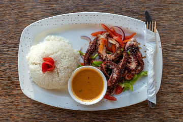 Fried octopus tentacles with white rice on a plate, close up