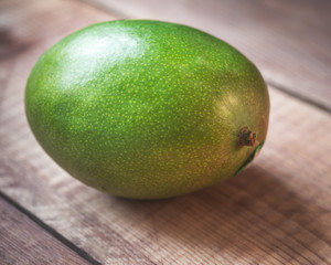 Green mango lies on a wooden table close-up,