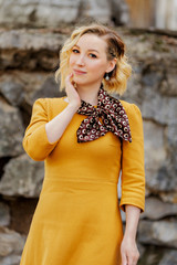 Fototapeta premium young attractive blonde in a mustard dress stands on the street and touches her face with her hands