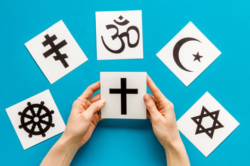 Choose religion concept. Hand with catholic cross near world religions symbols on blue background...