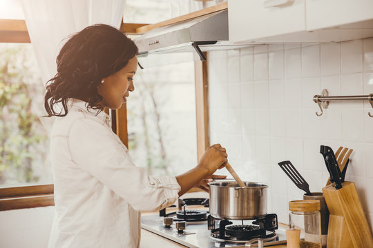 African American Black Woman Cooking Boiling Soup In The Kitchen At Home.