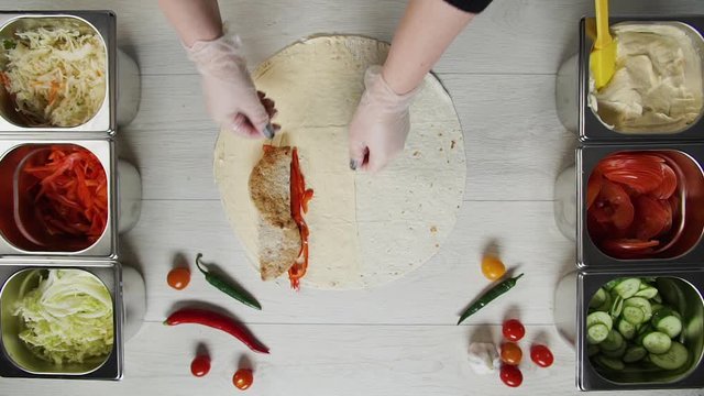 Top view of chef hands in white gloves puts beef cutlet on doner kebab shawarma in pita or lavash. Shawarma with chicken cutlet, pappers, cheese and vegetable