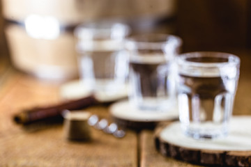 Fototapeta na wymiar Old rustic oak barrel and glasses of high quality distilled alcohol. Brazilian silver cachaça, called pinga, vodka, white rum, liqueur, pure drink, Poitín, sake, brandy or Absinthe.