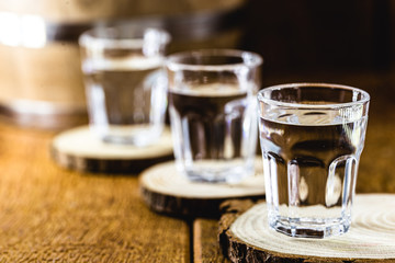 Old rustic oak barrel and glasses of high quality distilled alcohol. Brazilian silver cachaça, called pinga, vodka, white rum, liqueur, pure drink, Poitín, sake, brandy or Absinthe.