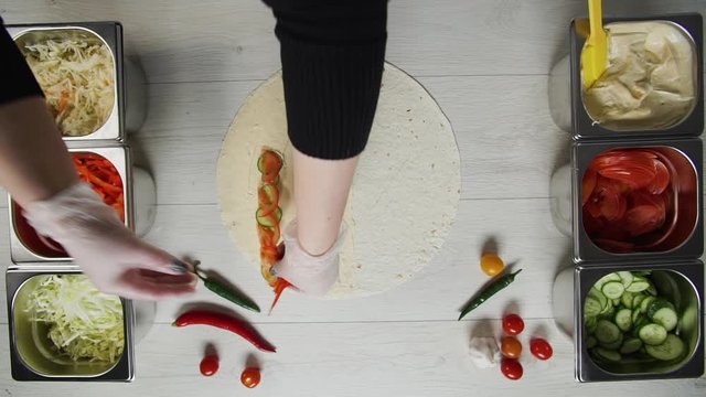 Top view of chef hands in white gloves puts peppres on doner kebab shawarma in pita or lavash. Shawarma with chicken cutlet, pappers, cheese and vegetable