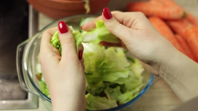 Static view of a womans hands ripping up pieces of lettuce and putting into a glass bowl for a salad