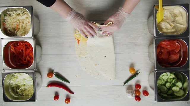 Top view of chef hands in white gloves wraps doner kebab shawarma in pita or lavash. Shawarma with chicken cutlet, pappers, cheese and vegetable