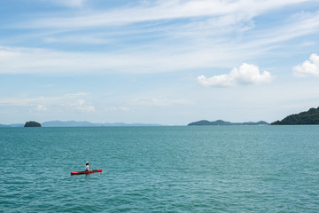 A woman kayaking on red kayak in emerald color water of Andaman sea with background of tropical island and copy space.
