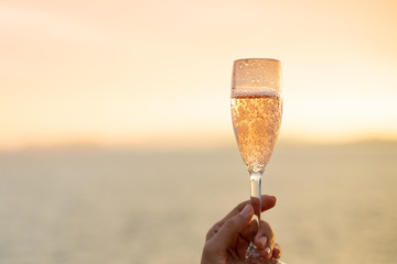 Woman on yacht hold a glass of sparkling wine in her hand with background of golden sunset moment to celebrate her life and happiness.