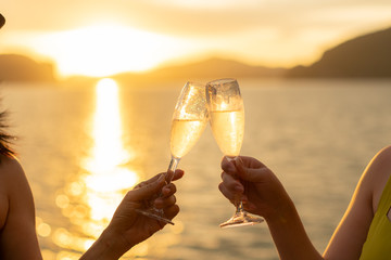 Women on yacht hold a glass of sparkling wine in her hand with background of golden sunset moment to celebrate her life and happiness.