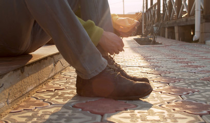 Close up male hands tying shoelaces on boots. A young man sitting in the tiled courtyard of a...