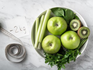 Green fruits and vegetables for making detox smoothie. Apples, kiwi, spinach, celery and parsley on a light background. Top view.