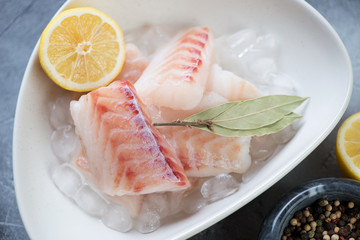 Close-up of raw fresh codfish fillet on ice with bay leaves and lemon, selective focus, studio shot