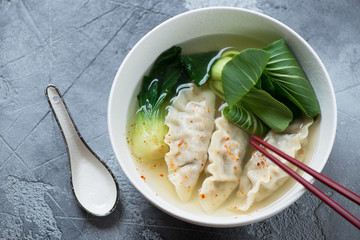 Bowl of asian soup with dumplings and pak-choi, elevated view on a grey concrete background, horizontal shot