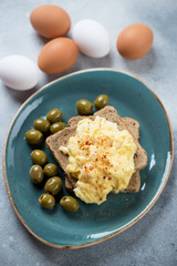British style scrambled eggs with bread slices and olives served on a turquoise plate, vertical shot