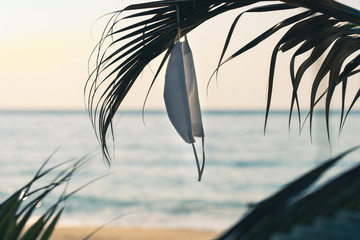 Hygienic mask hanging on palm leaves on the beach against the sea