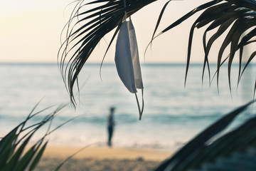 Hygienic mask hanging on palm leaves on the beach against the sea