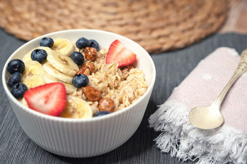 Cooked oatmeal with banana, blueberry, strawberry and nuts in white bowl