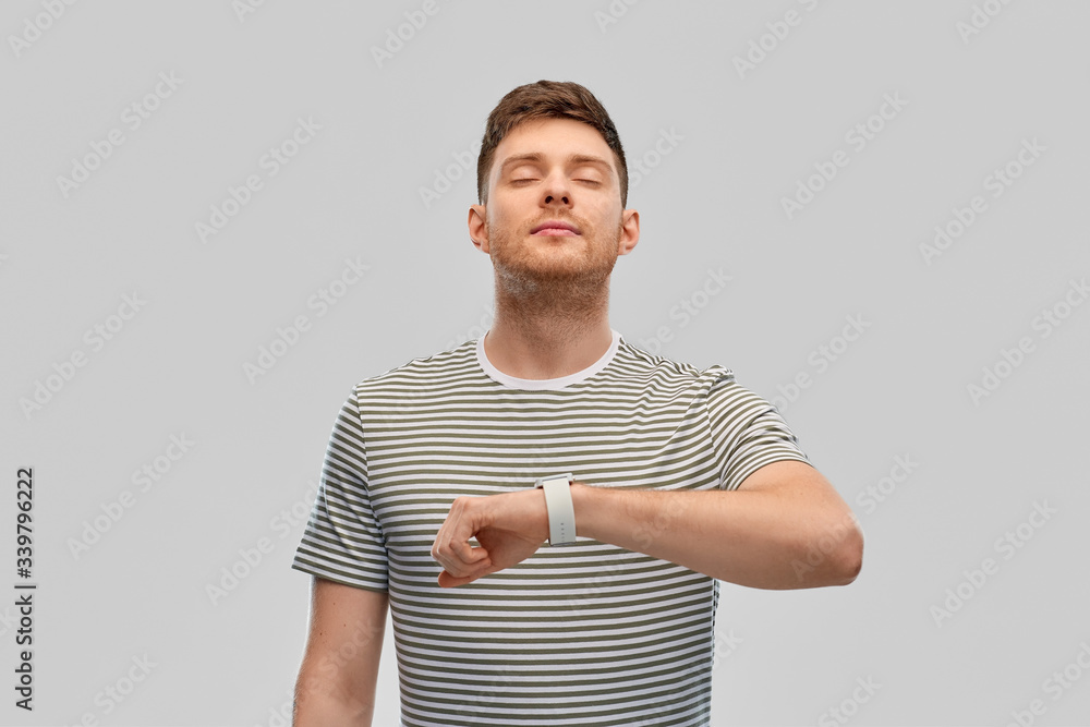 Wall mural technology, relax and people concept - calm young man with smart watch meditating over grey background