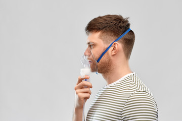 health, medical equipment and people concept - unhealthy young man wearing oxygen mask over grey...