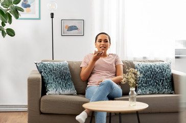 people, technology and communication concept - happy young african american woman using voice command recorder on smartphone at home