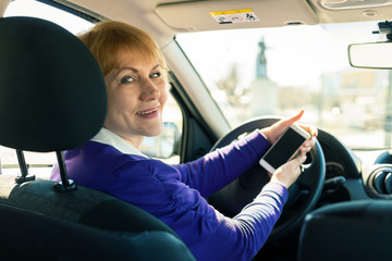 A woman sits in a car behind the wheel and looks at the road