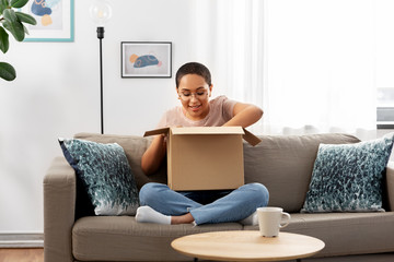 delivery, shipping and people concept - happy young african american woman opening parcel box at home