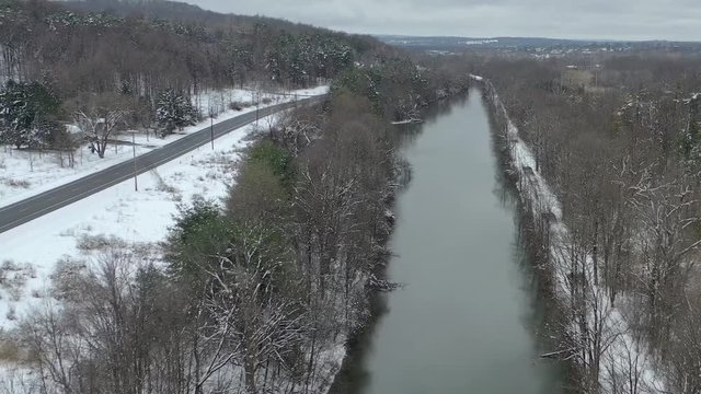 Flying over river next to highway with light traffic in winter on cloudy day. Dolly out aerial.