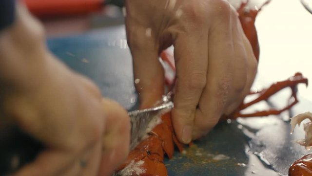 Cutting a cooked lobster in half with a sharp knive by a professional chef in a kitchen