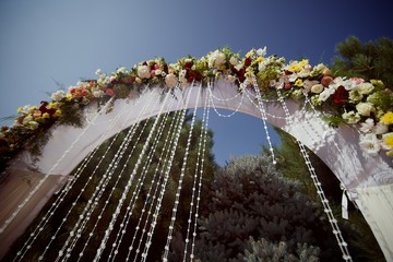 Bright stylish beautiful wedding arch with fresh flowers against the sky