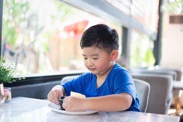 Asian boy eating cake in bakery shop or cafe.