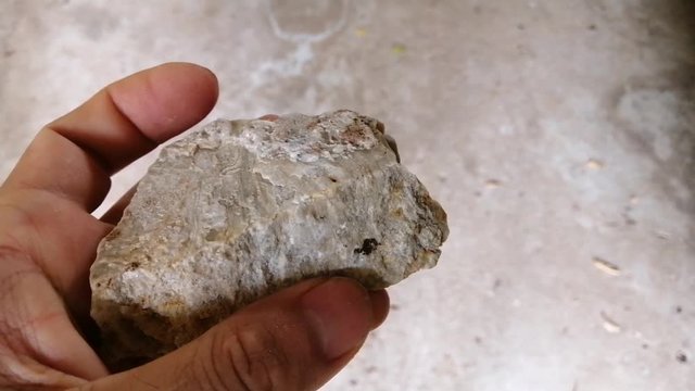 Feldspar stone in a hand. There is noise and grain caused by the texture of stone. Feldspar, any of a group of aluminosilicate minerals that contain calcium, sodium, or potassium.
