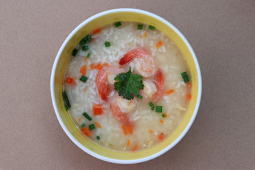 Rice congee mixed with shrimp in the round bowl. Sprinkled with spring onions and coriander.