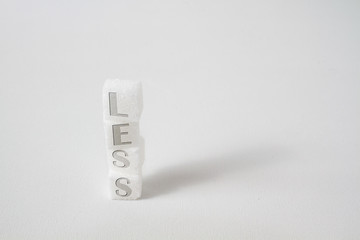 high-key macro of stapled sugar cubes with the word "less" written on the square blocks promoting a more healthy diet