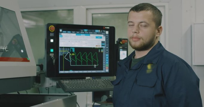 mechanical technician operative of cnc milling cutting machine working at computer at tool workshop, looks into the monitor. Filmed on RED EPIC-W 4K camera.