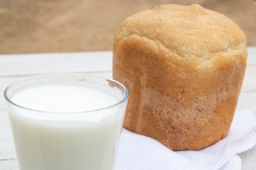 Fresh homemade bread and a glass of natural homemade organic yogurt on a white wooden background.