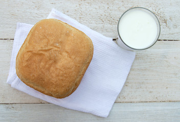 Fresh homemade bread and a glass of natural homemade organic yogurt on a white wooden background.