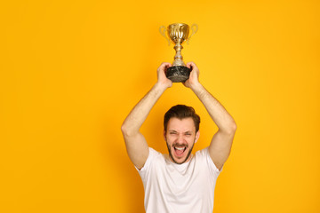 A young sportsman on yellow background, smiling happily, shouting out loud, holding a golden prize...