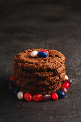 Homemade oat chocolate cookies stack with cereal with juicy jelly beans on textured dark black background, angle view