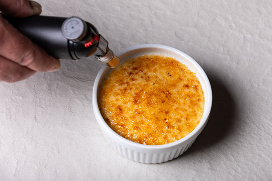 Chef making a crème brulee in a small white bowl with torch flame