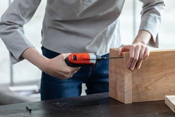 自宅にて電動ドライバーでネジを木に打つ女性の手元