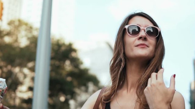 Portrait of young happy woman in sunglasses walking in downtown and eating, holding the melting ice cream with topping.