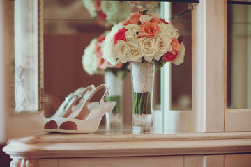 Bouquet of bride with roses stands next to white heels on white boudoir table