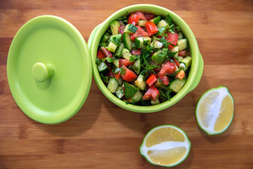 Chopped cucumber tomato salad in a green bowl. Lemon cut in half . fresh vegetable salad with tomato, cucumber and green onion on Cutting board.