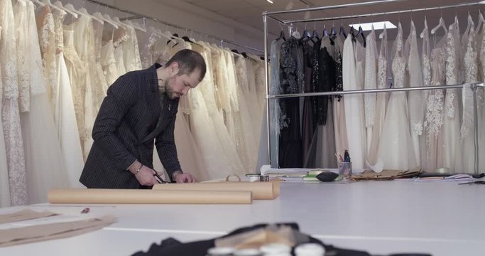 The fashion designer cutting a tissue curve on desktop in evening dress atelier