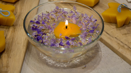 Burning heart-shaped candle floating in bowl with water and mauve flowers