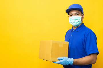 Delivery man blue uniform wearing rubber gloves and mask holding parcel cardboard box on yellow...