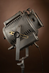 A close-up photo of a metal illuminating spotlight with all details and sensations of the 80s on chocolate brown background