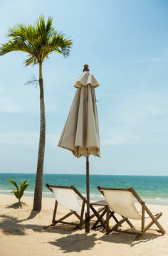 Two deckchair umbrella and coconut tree facing out sea on idyllic beach	