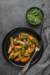 Kartoffelspalten mit Pesto aus Kohlrabiblättern auf einem dunklen Hintergrund